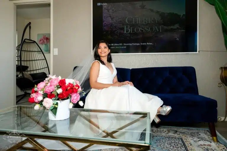 A beautiful bride in her wedding gown sitting on a navy-blue sofa, surrounded by vibrant floral decor, as she prepares for her wedding day in Wellington, New Zealand.