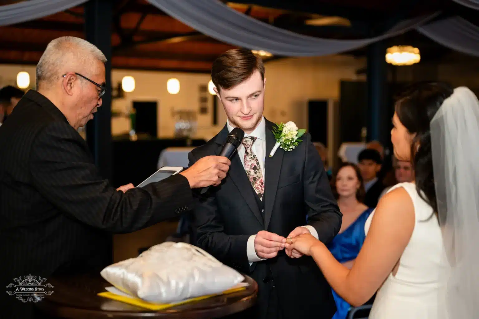 The groom placing the wedding ring on the bride's finger during the ceremony, with the celebrant officiating.