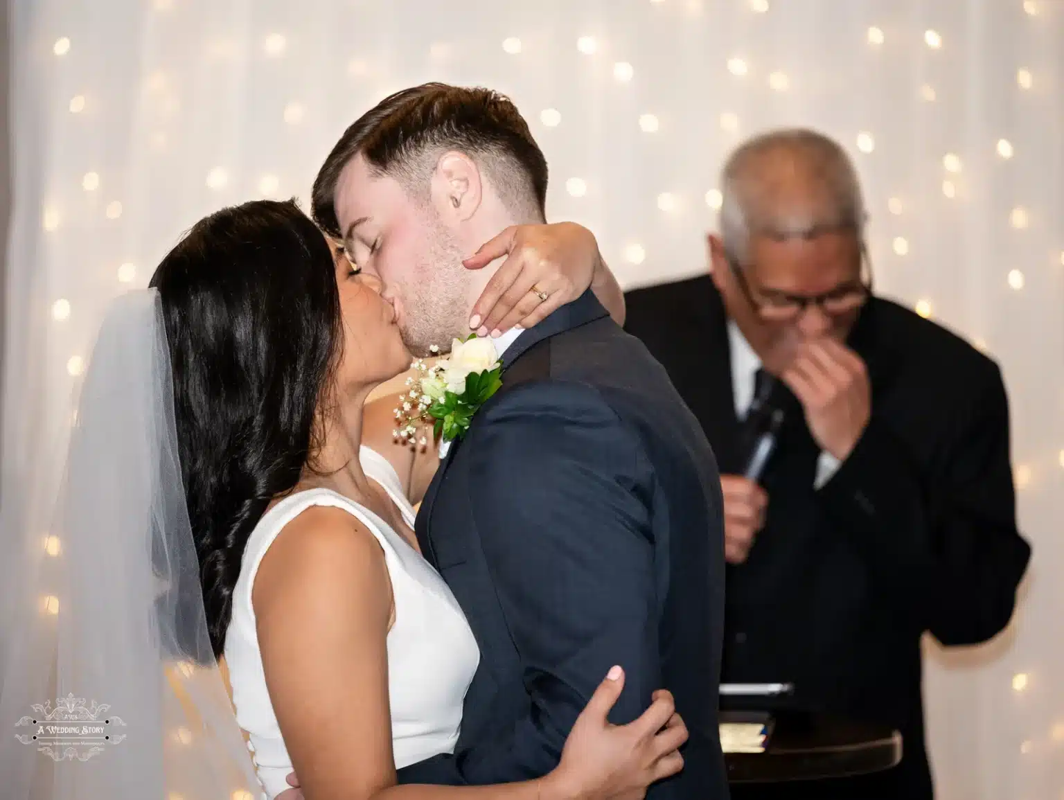 Bride and groom share a heartfelt first kiss during their wedding ceremony in Wellington, illuminated by soft fairy lights.