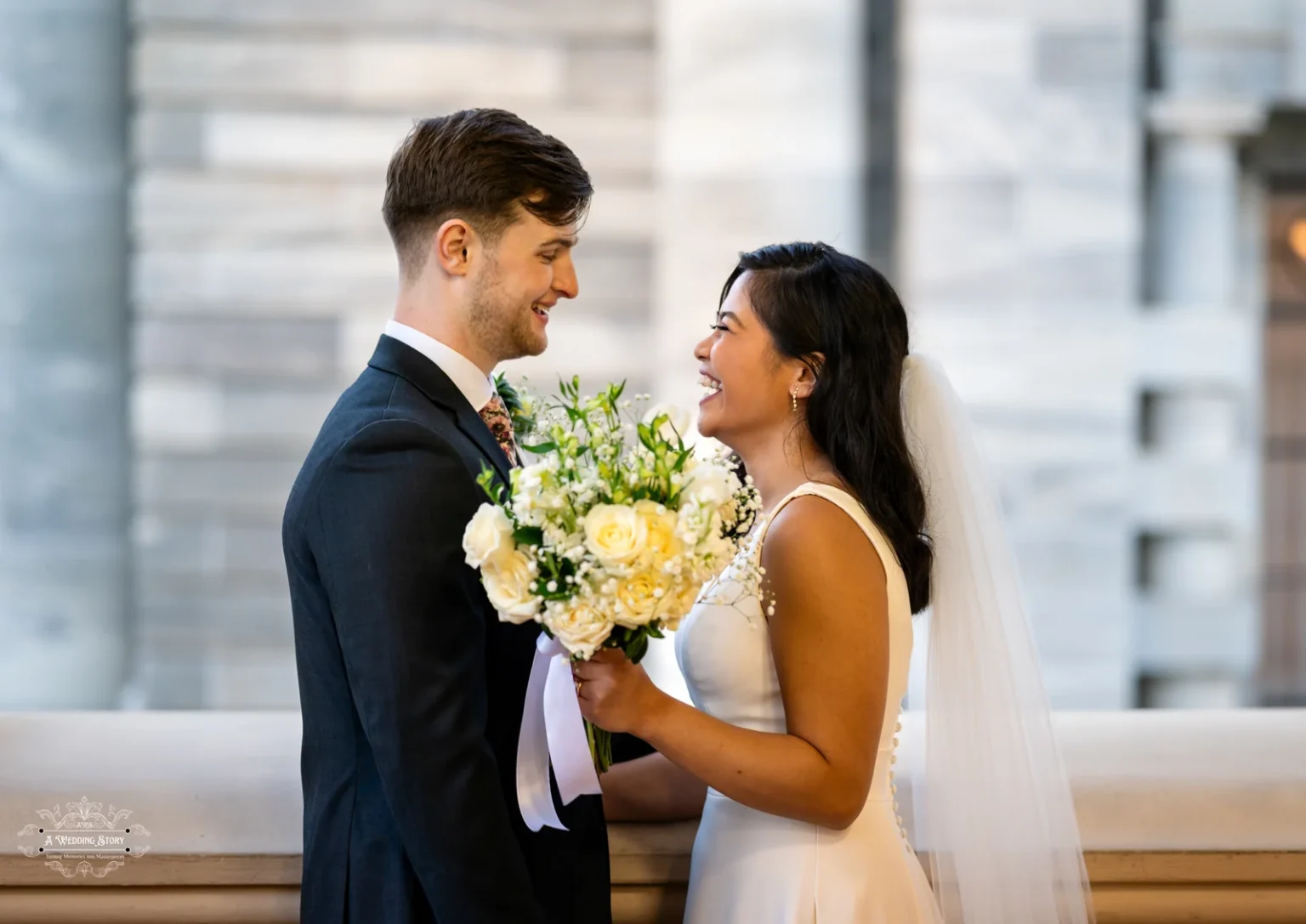 A happy bride and groom smiling at each other while holding a bouquet of white and yellow roses in Wellington, New Zealand.