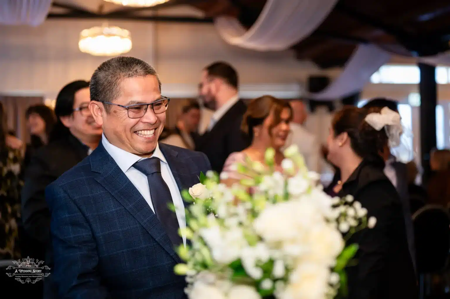 Smiling guest in a navy suit holding white floral bouquet at a wedding reception in Wellington, New Zealand.