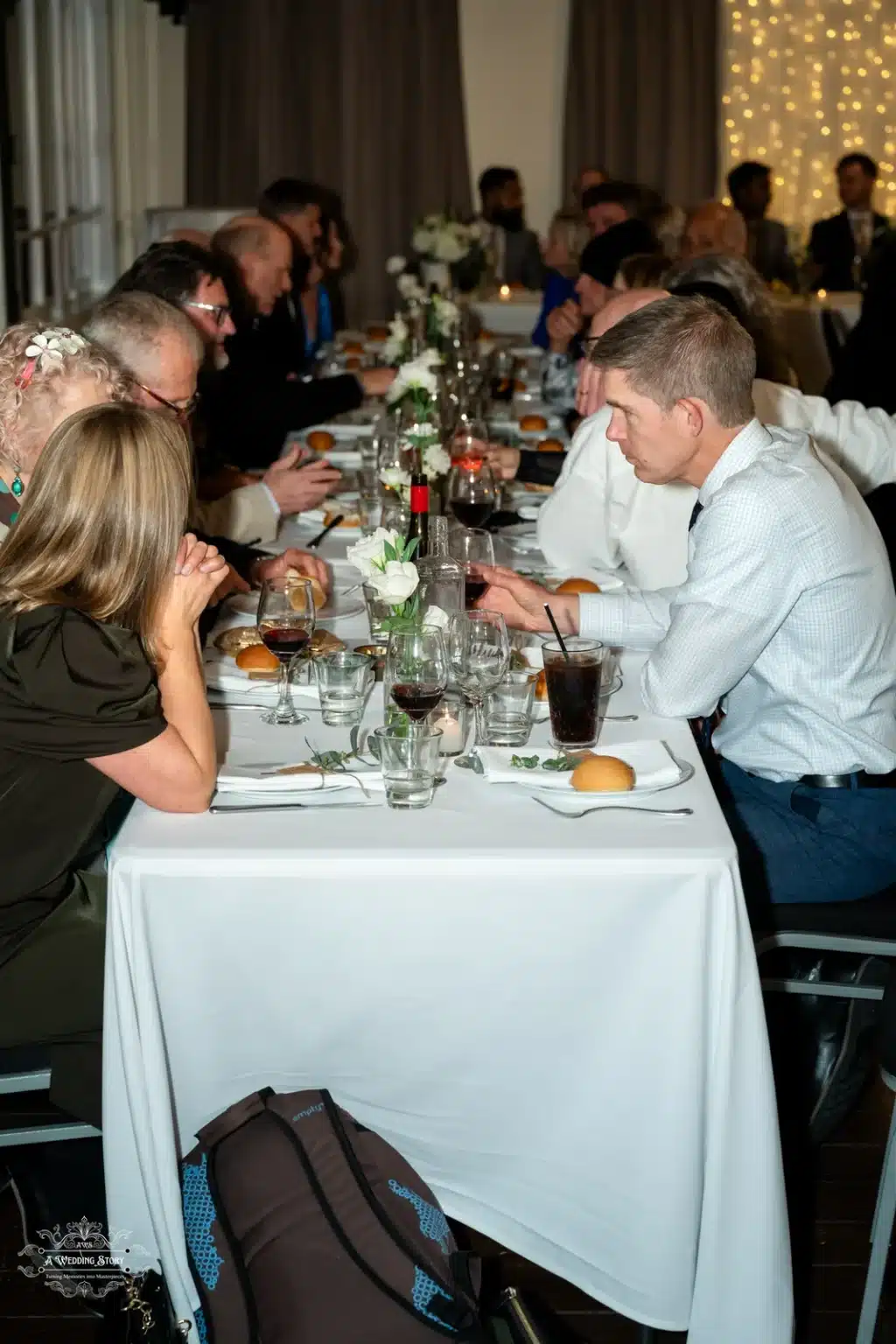 Wedding guests enjoying their meal during the reception, seated at a long table with drinks and food.