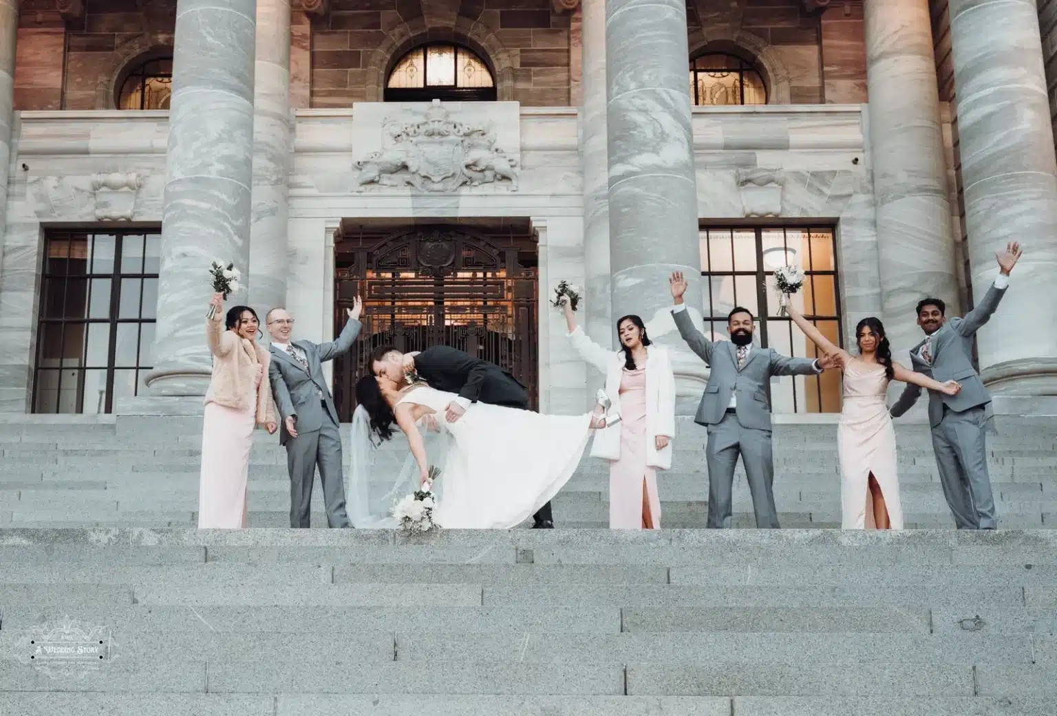 Bride and groom share a romantic dip as their wedding party cheers on the grand steps of Parliament.