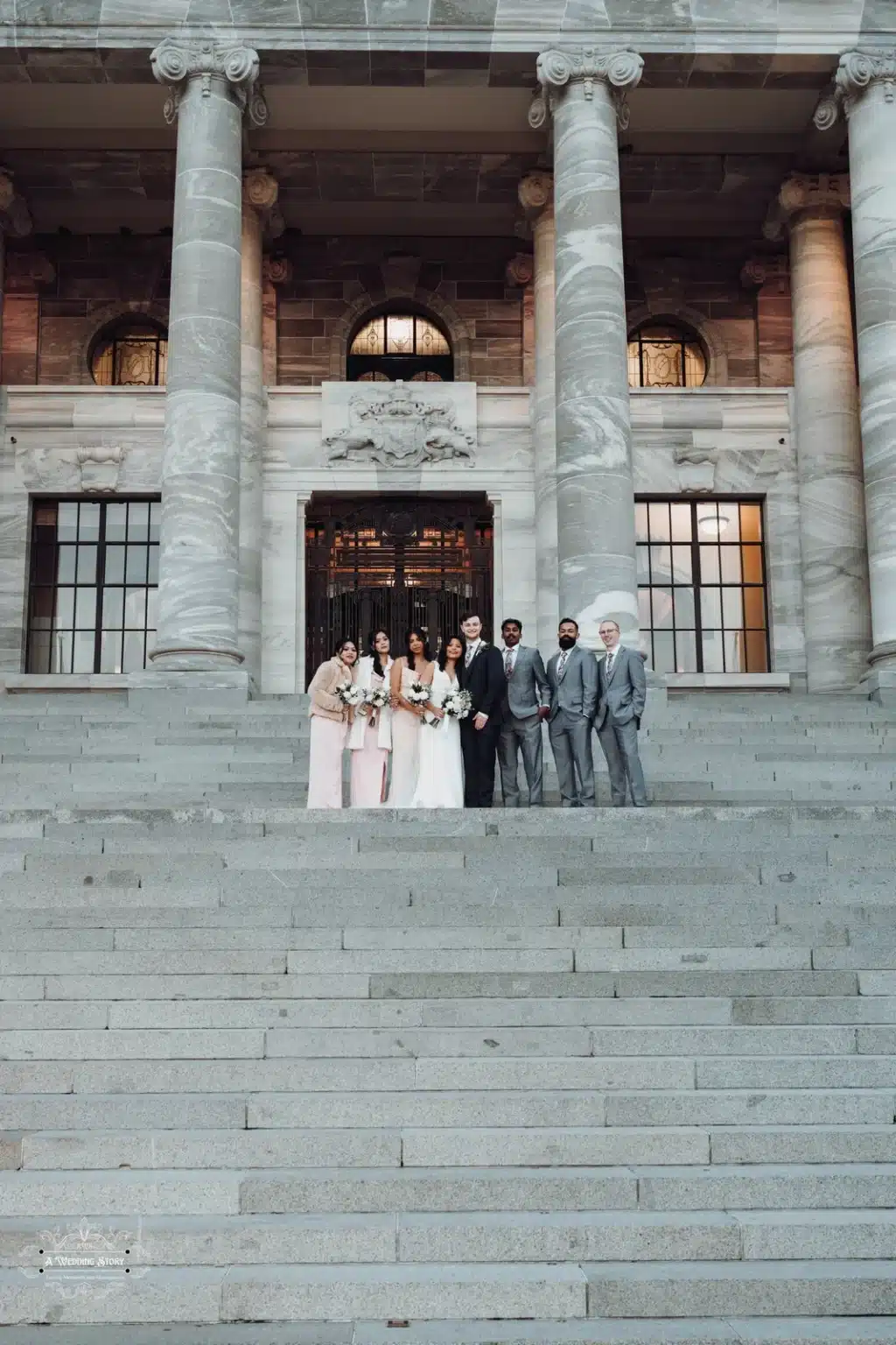 Bride, groom, and wedding party pose on the iconic Parliament steps, surrounded by grand architectural columns.