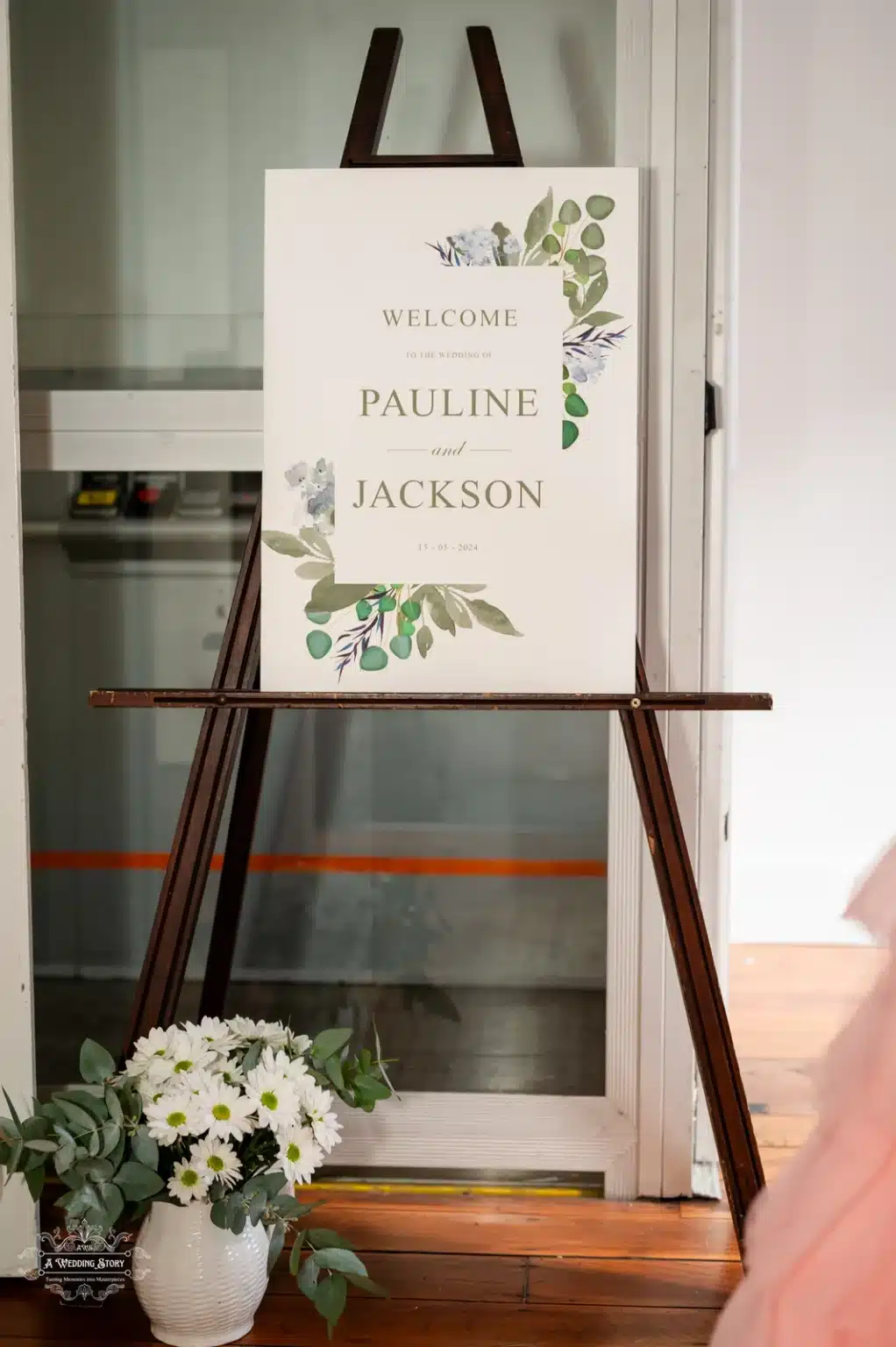 A beautifully designed wedding welcome sign for Pauline and Jackson, adorned with green foliage accents, placed on an easel with a floral arrangement nearby in Wellington, New Zealand.