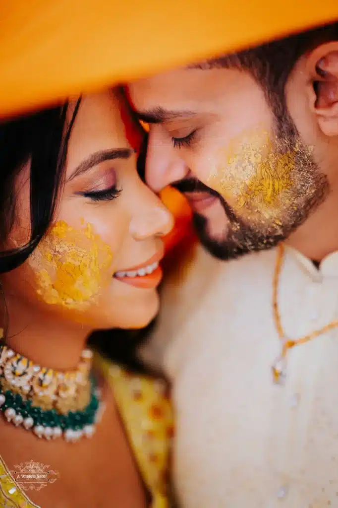 Close-up of a couple during a Haldi ceremony, with vibrant yellow turmeric smeared on their cheeks, smiling and touching foreheads in an intimate, joyful moment. Traditional Indian wedding rituals, Gujarati couple in love, Haldi function photography by A Wedding Story, New Zealand