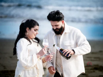 Bride and groom celebrating their elopement on a beach in Wellington, pouring champagne together