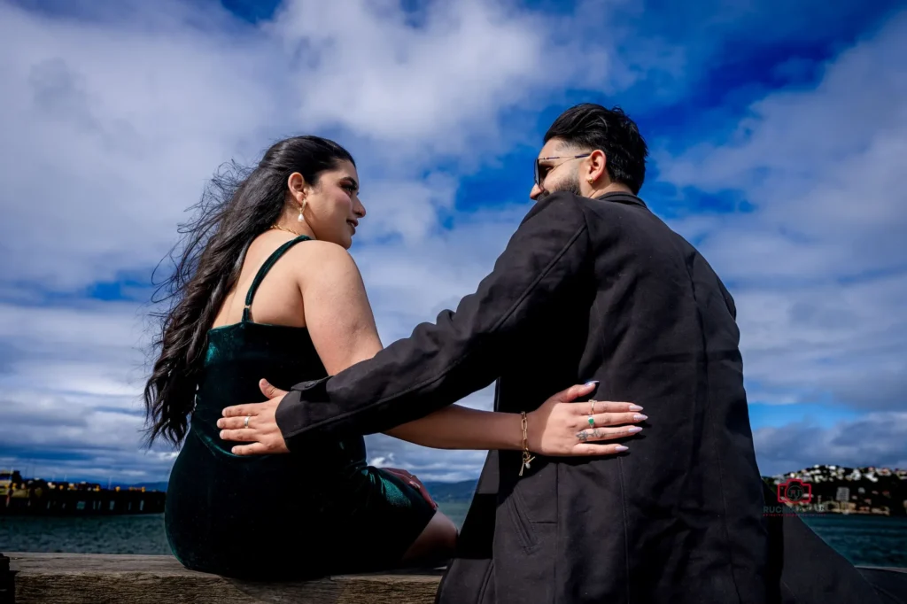 Couple sitting by the seaside, gazing at each other under a vibrant blue sky in Wellington