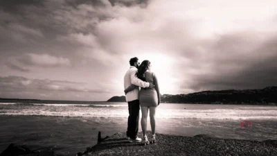 Couple embracing on a beach at sunset, gazing into the horizon in a black-and-white elopement photo