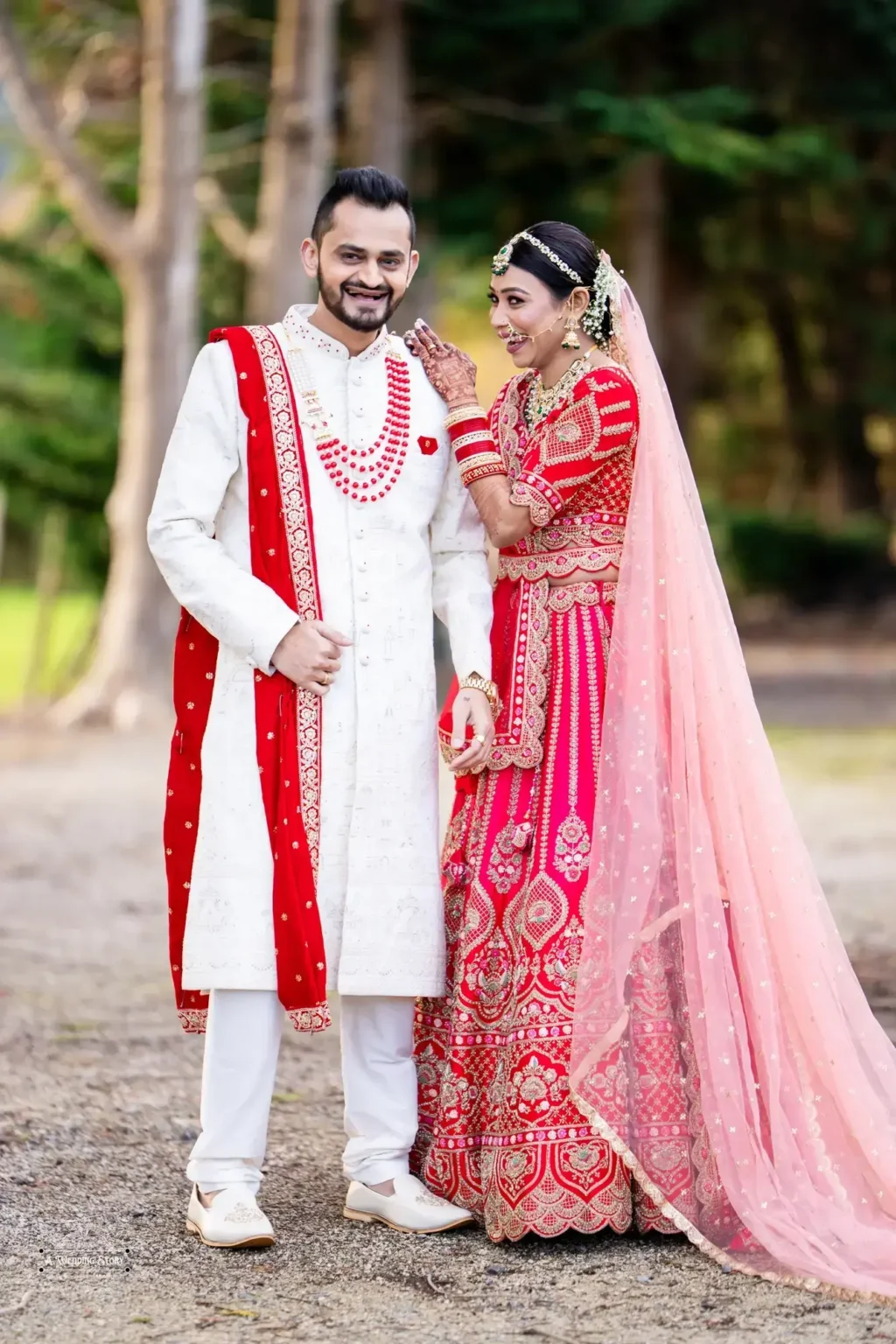 Gujarati bride in a red lehenga and groom in a white sherwani sharing a joyful moment during their wedding photoshoot in Wellington, New Zealand