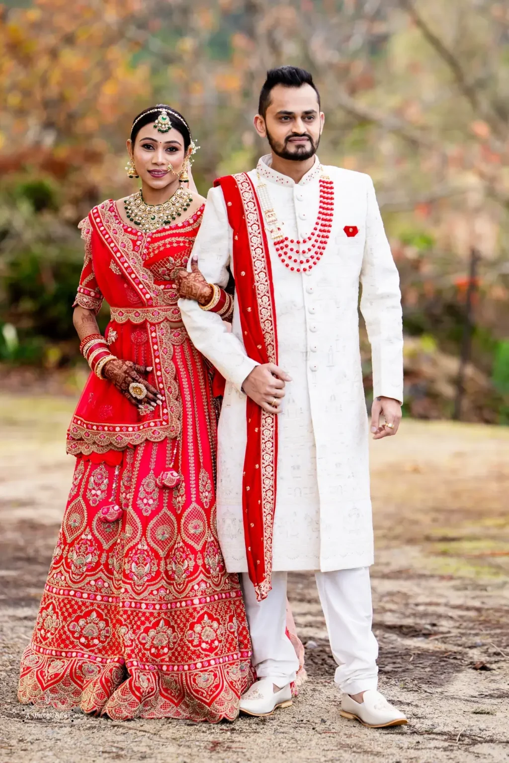 Gujarati bride in a red lehenga and groom in a white sherwani posing together during their wedding photoshoot in Wellington, New Zealand