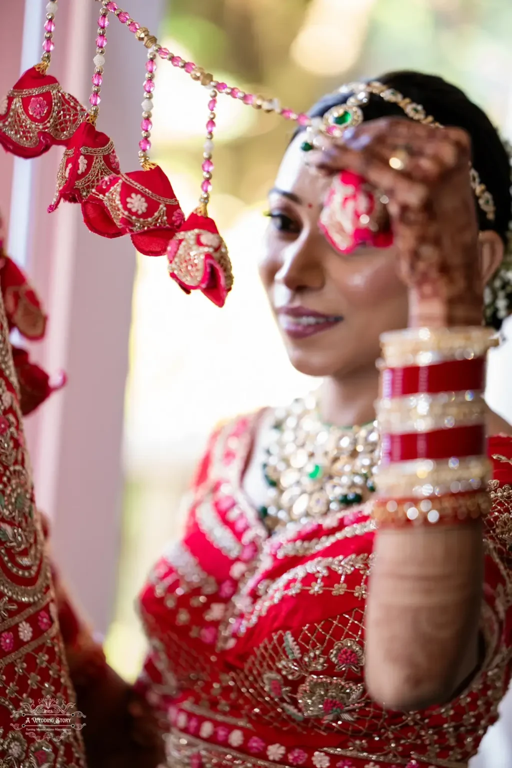 A close-up of a Gujarati bride in a vibrant red lehenga, holding traditional kalire adorned with intricate golden embroidery, captured in soft natural light.