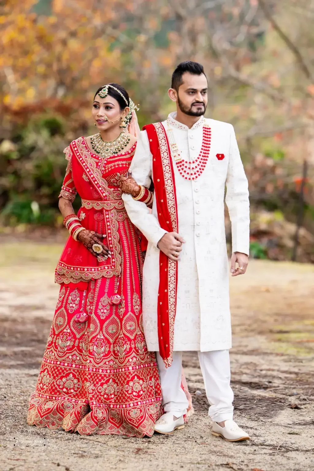 Gujarati bride in a traditional red lehenga and groom in a white sherwani walking arm-in-arm during their wedding photoshoot in Wellington, New Zealand