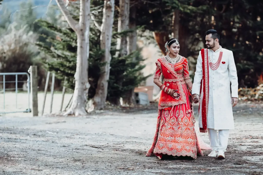 Indian bride and groom in traditional wedding attire walking hand in hand outdoors in Wellington, New Zealand