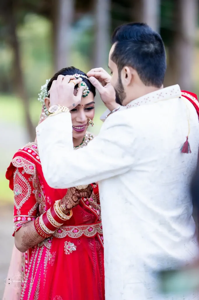 Groom adorning the bride with a traditional mang tikka during their Gujarati wedding ceremony in Wellington, New Zealand