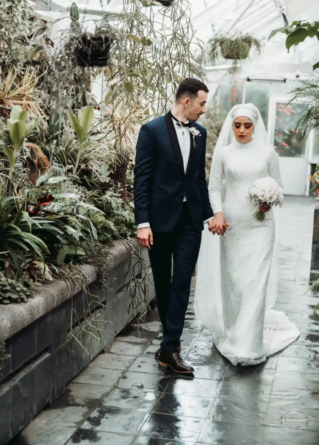 Afghan bride in a white hijab and groom in a tuxedo holding hands, walking together through a lush botanical garden on their wedding day in Wellington.