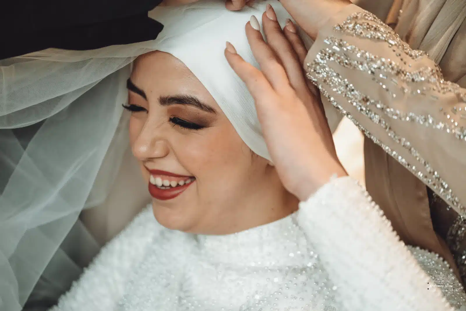 Smiling Afghan bride wearing a white hijab, assisted by friends or family with final touches before her wedding in Wellington.