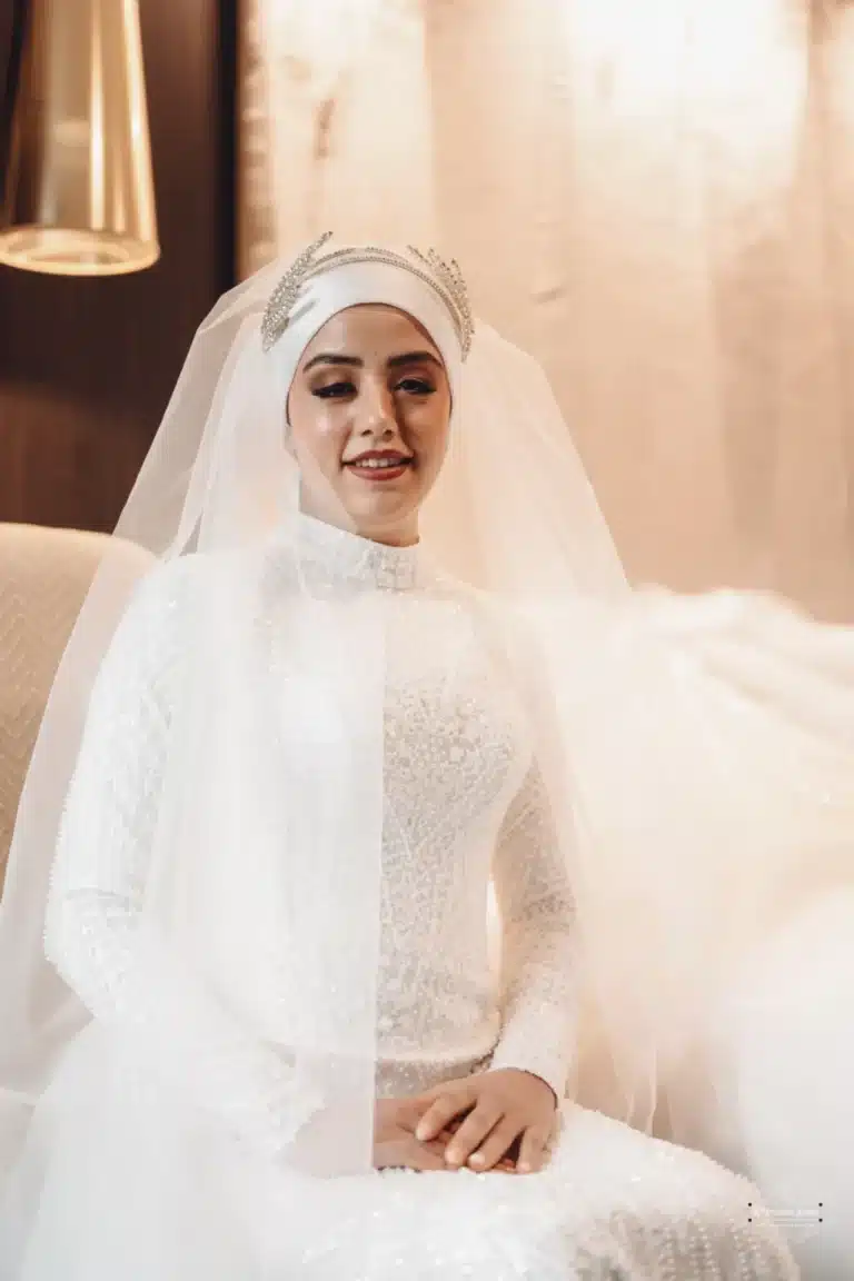 Afghan bride in a beaded white gown with a traditional headpiece, seated and smiling during her wedding day in Wellington.