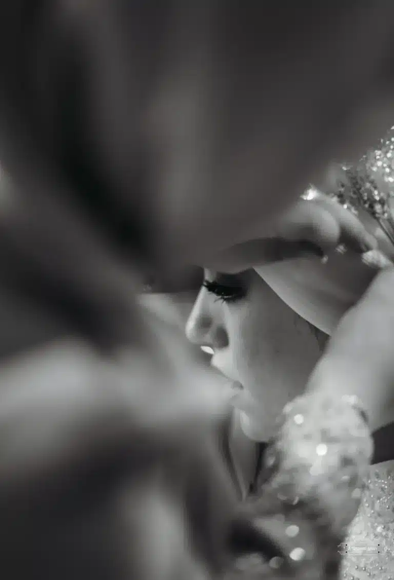 Black and white close-up of an Afghan bride’s profile with hands adjusting her headpiece during wedding preparations in Wellington.