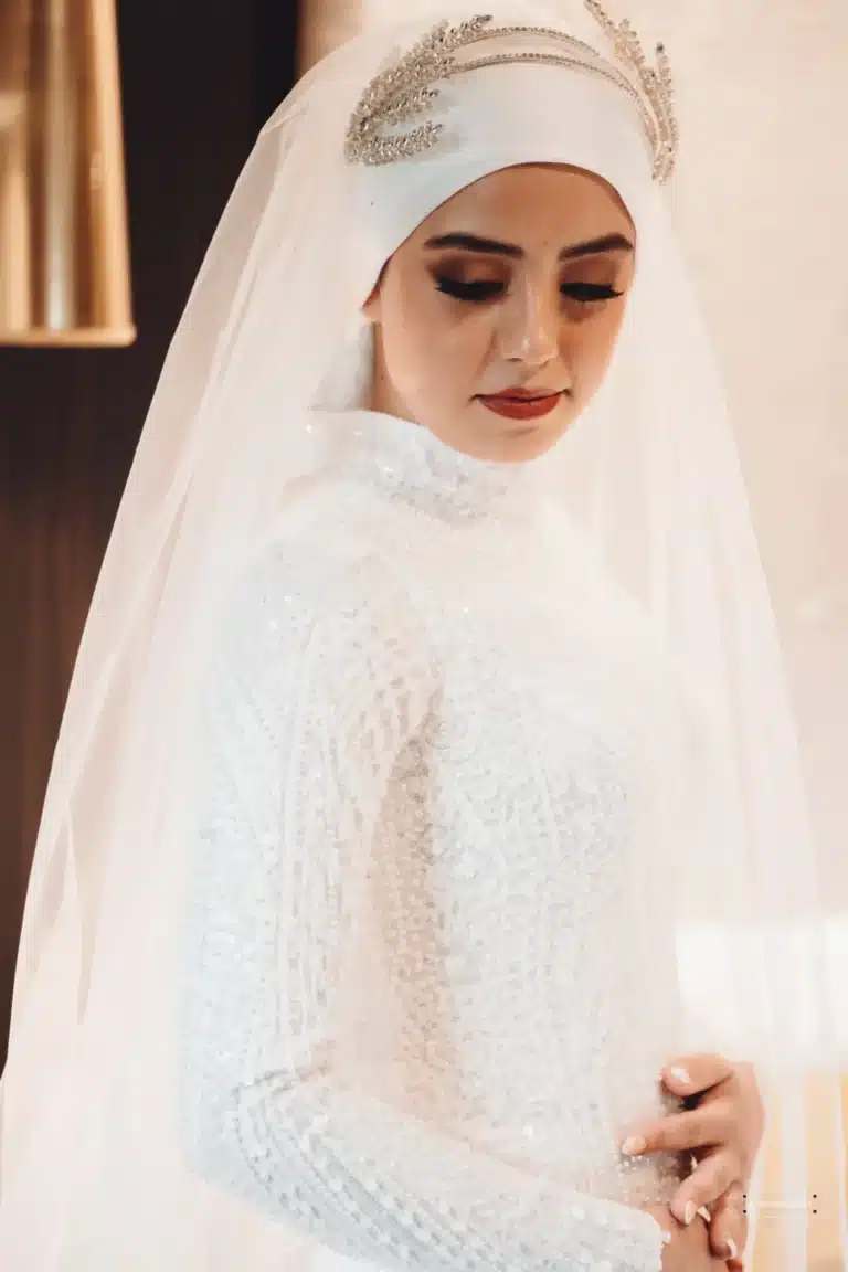 Afghan bride in a white, intricately beaded gown with a traditional headpiece, looking down gracefully during her wedding day in Wellington.