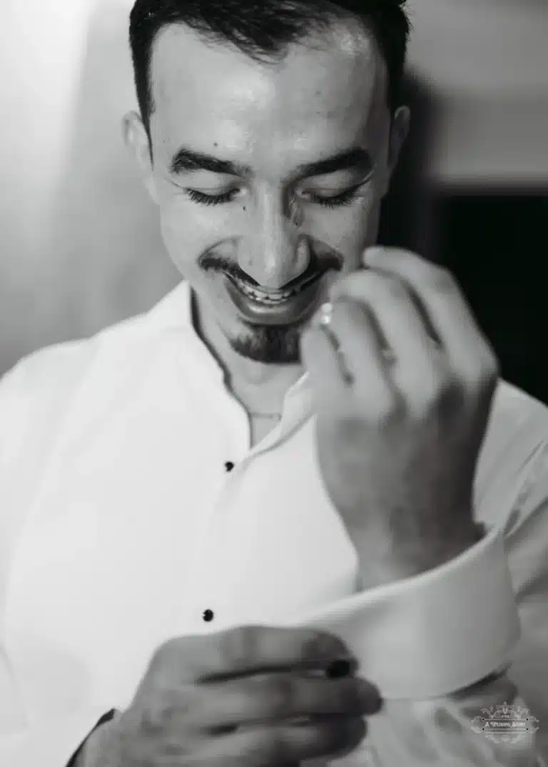 Afghan groom smiling while adjusting his cufflink, captured in a candid black-and-white portrait before his wedding in Wellington.