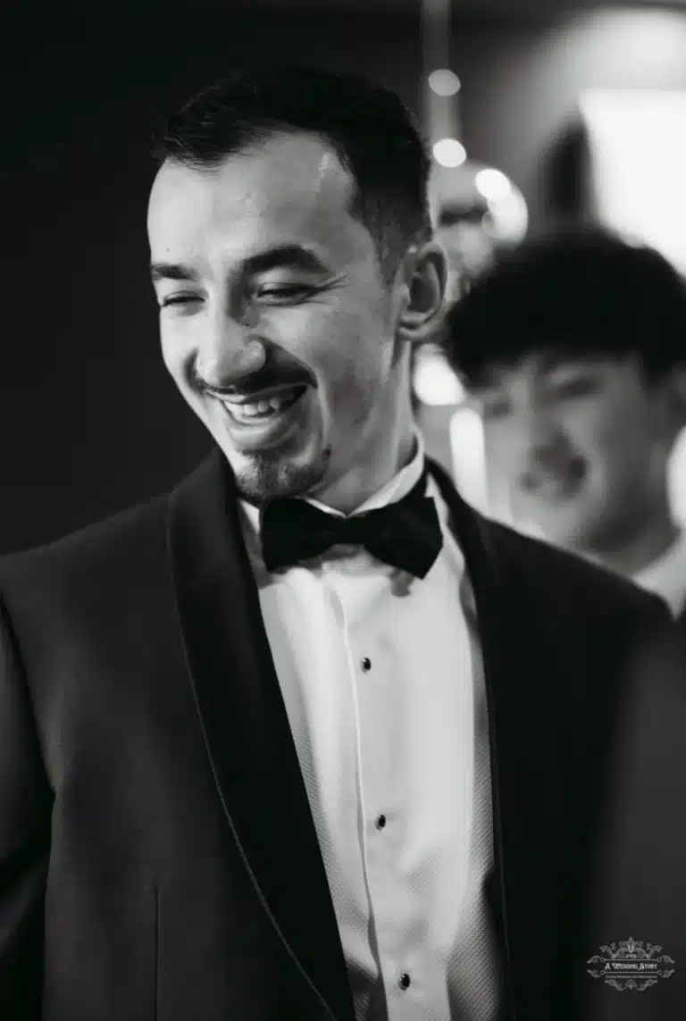 Afghan groom in a tuxedo smiling with joy, captured in a candid black-and-white moment before his wedding in Wellington.