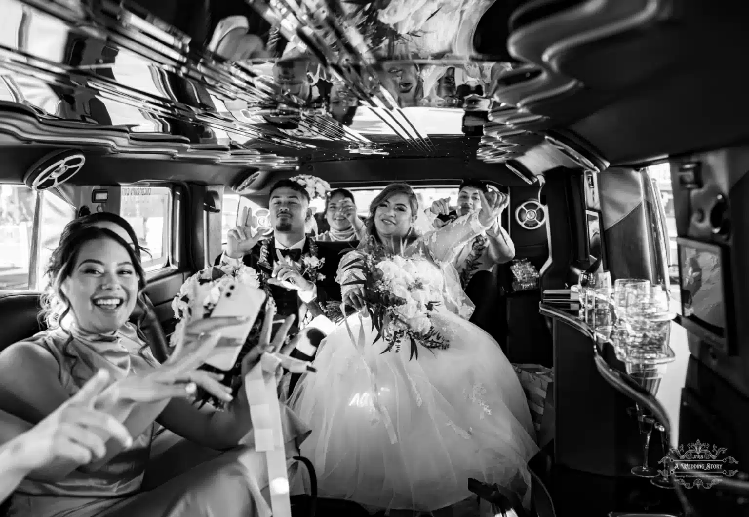 Bride and groom with friends enjoying a celebratory moment inside a wedding limousine, sharing laughter and gestures of joy in a stylish black-and-white setting.