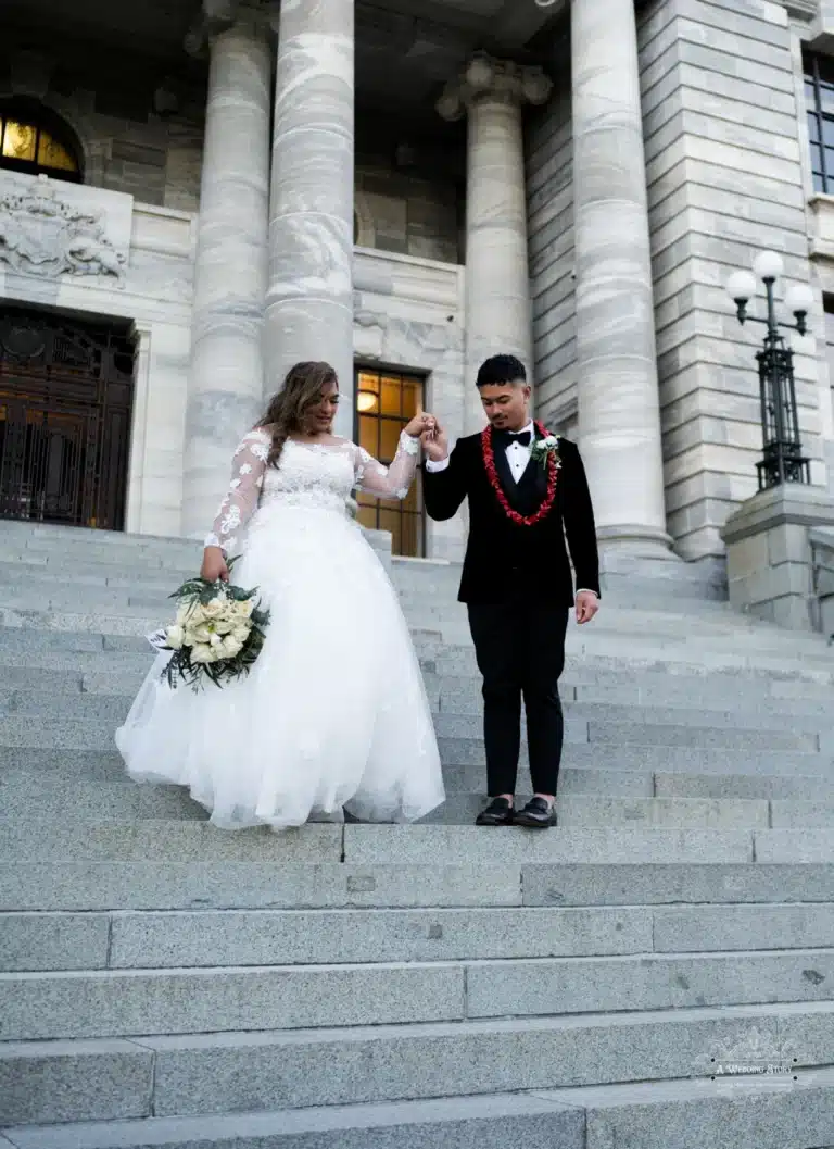 Bride and groom holding hands as they gracefully descend the steps of a historic landmark during a wedding photoshoot in Wellington, New Zealand.