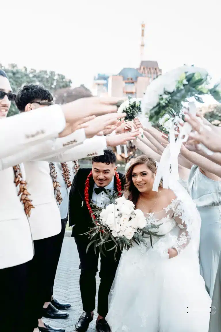 Bride and groom smiling as they walk under an arch of raised bouquets created by their bridal party during a fun wedding photoshoot in Wellington, New Zealand.