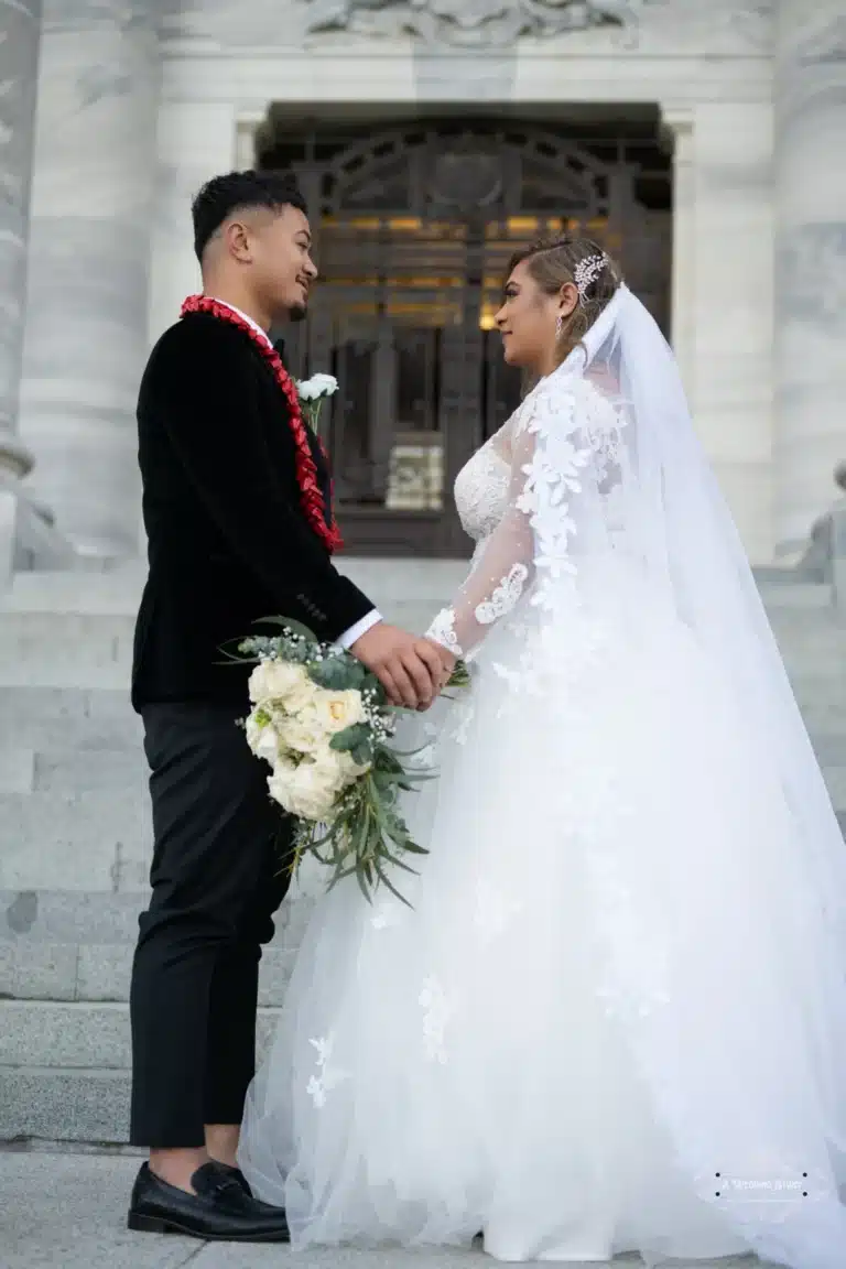 Bride and groom share a loving moment, holding hands during a wedding photoshoot at a historic location in Wellington, New Zealand.