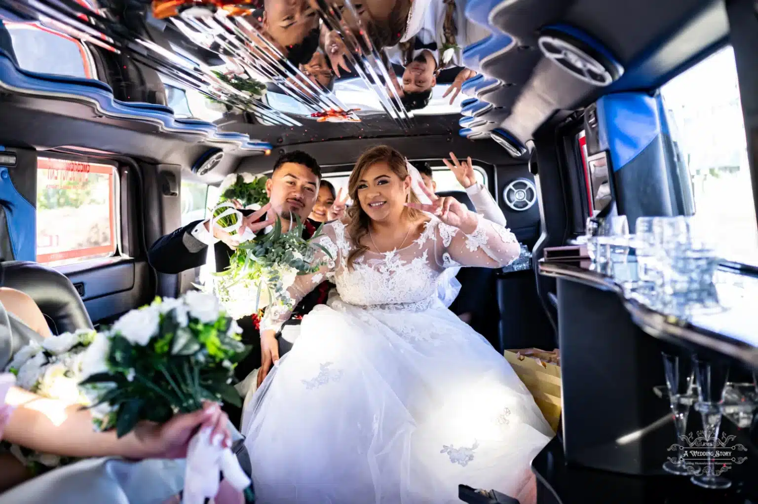 The bride and groom joyfully flash peace signs while surrounded by their wedding party inside a decorated limousine, capturing a moment of excitement and celebration.