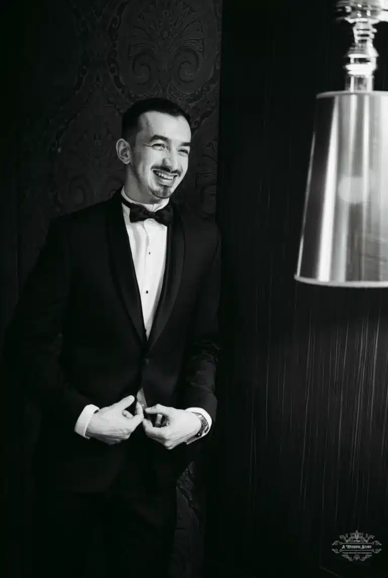 Black and white image of the groom smiling as he adjusts his suit jacket, exuding confidence and joy before his wedding ceremony.