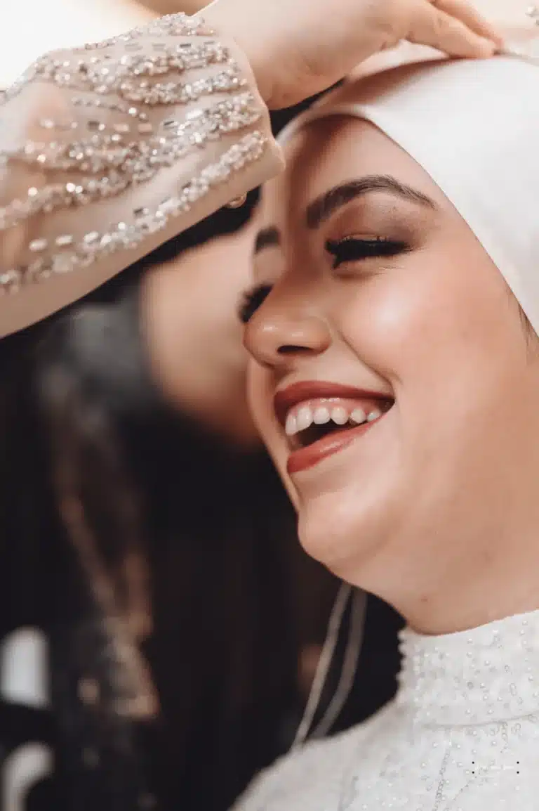 Close-up of Afghan bride smiling brightly as a loved one adjusts her headpiece during wedding preparations in Wellington.F