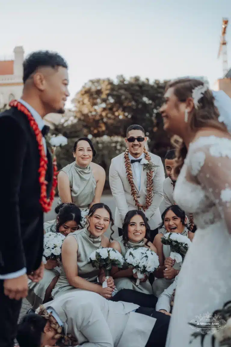 Bride and groom share a lighthearted moment surrounded by a joyful bridal party during a wedding photoshoot in Wellington, New Zealand.