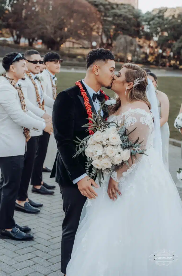 Bride and groom share a romantic kiss during their wedding ceremony, surrounded by their bridal party in Wellington, New Zealand.