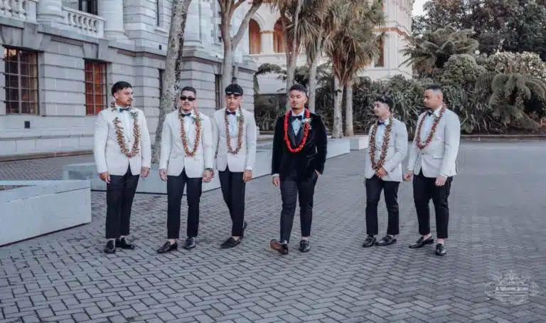 Groom and his groomsmen striking a stylish pose on the steps of a historic landmark in Wellington, New Zealand, during a wedding photoshoot. Groom and groomsmen walking together in stylish attire with traditional accessories during a wedding photoshoot in Wellington, New Zealand.