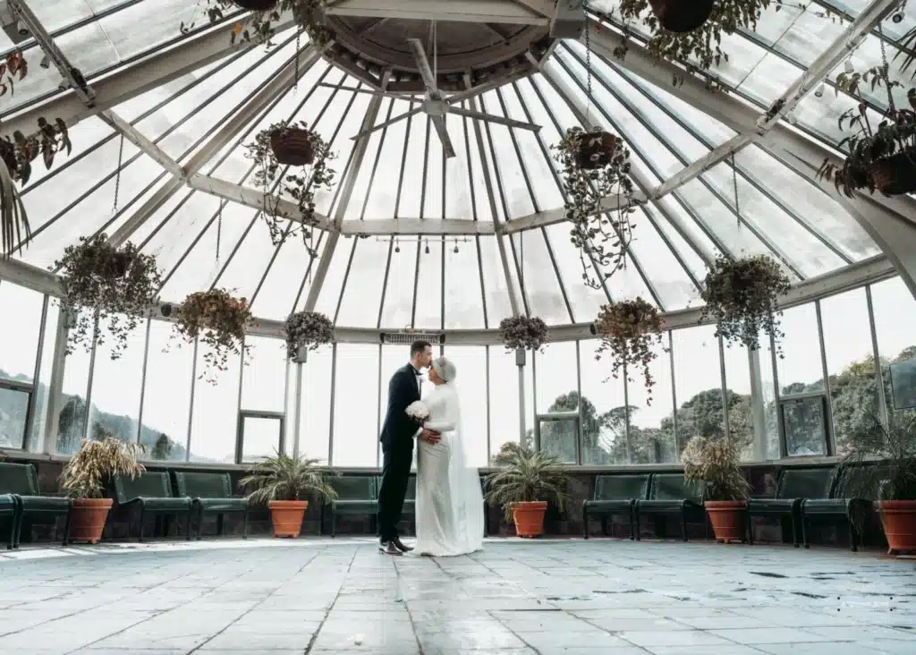 Bride and groom embracing under the glass dome of Wellington Indian Cultural Centre, Kilbirnie, during their Afghan wedding