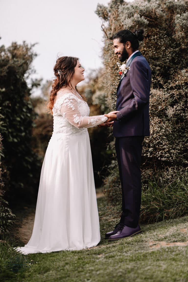 A couple holding hands and sharing a loving gaze surrounded by greenery during their Boomrock wedding in Wellington.