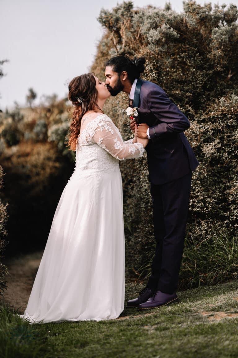 A couple sharing a romantic kiss surrounded by lush greenery during their Boomrock wedding in Wellington.