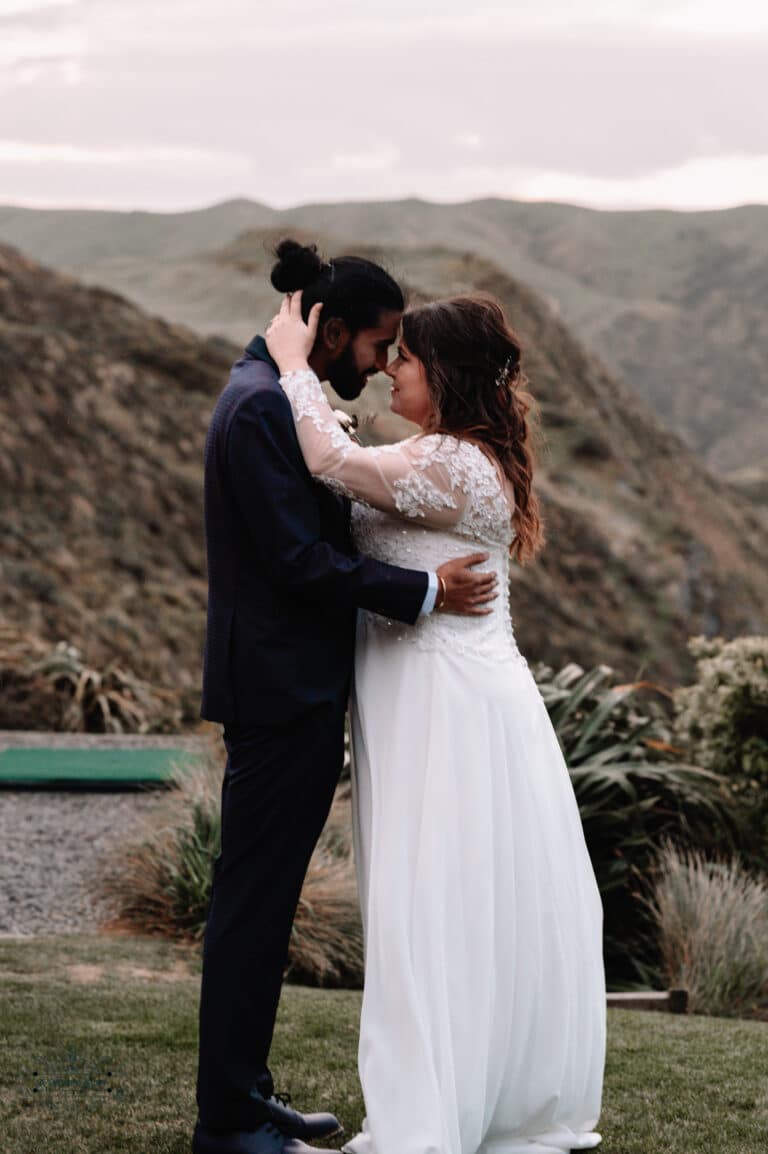 A romantic moment between a couple on their wedding day at Boomrock, Wellington, with scenic hills in the backdrop.