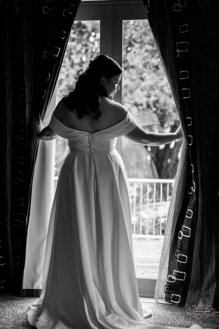 Black and white portrait of a bride looking out the window before her wedding in Carterton, New Zealand