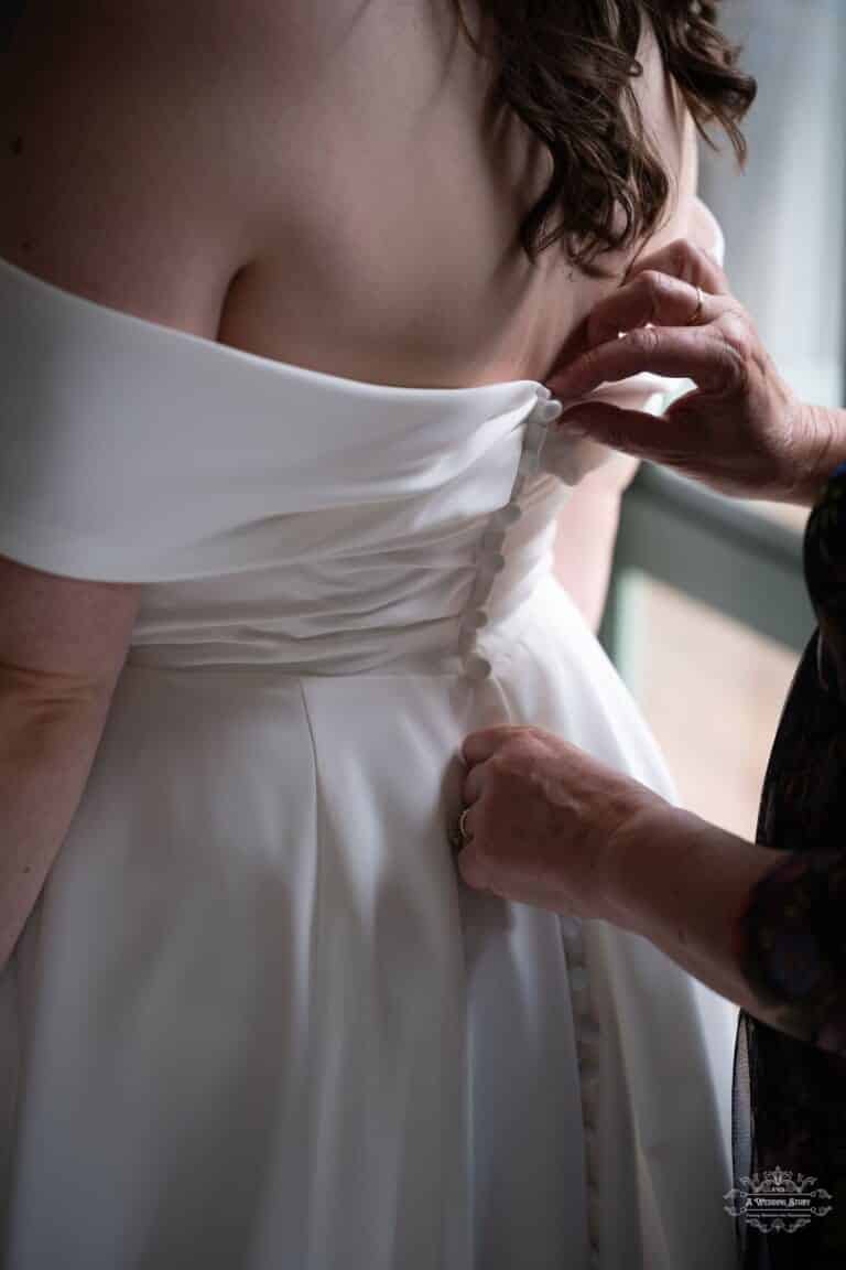 A close-up of hands buttoning the bride’s wedding dress, capturing a heartfelt pre-ceremony moment