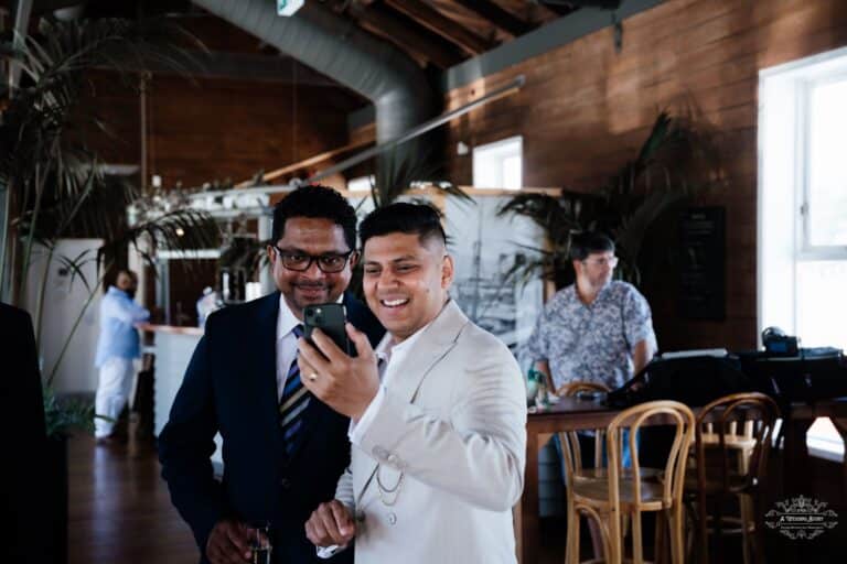 Wedding guests sharing a joyful moment while capturing memories on a phone during an intimate wedding celebration, photographed by a Wellington wedding photographer