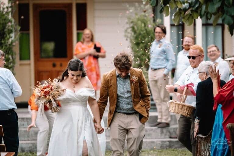 Bride and groom walk hand in hand as guests throw confetti in celebration at their wedding venue