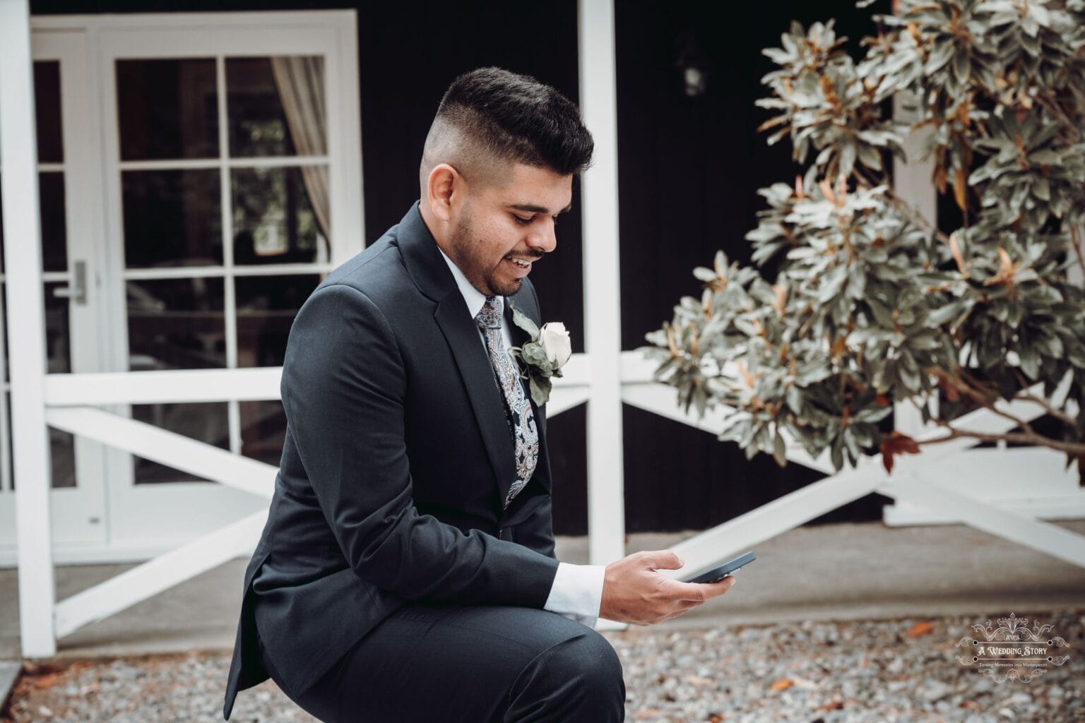 A candid shot of the groom smiling as he checks his phone, surrounded by the charming rustic setting of The Lodge in Wellington