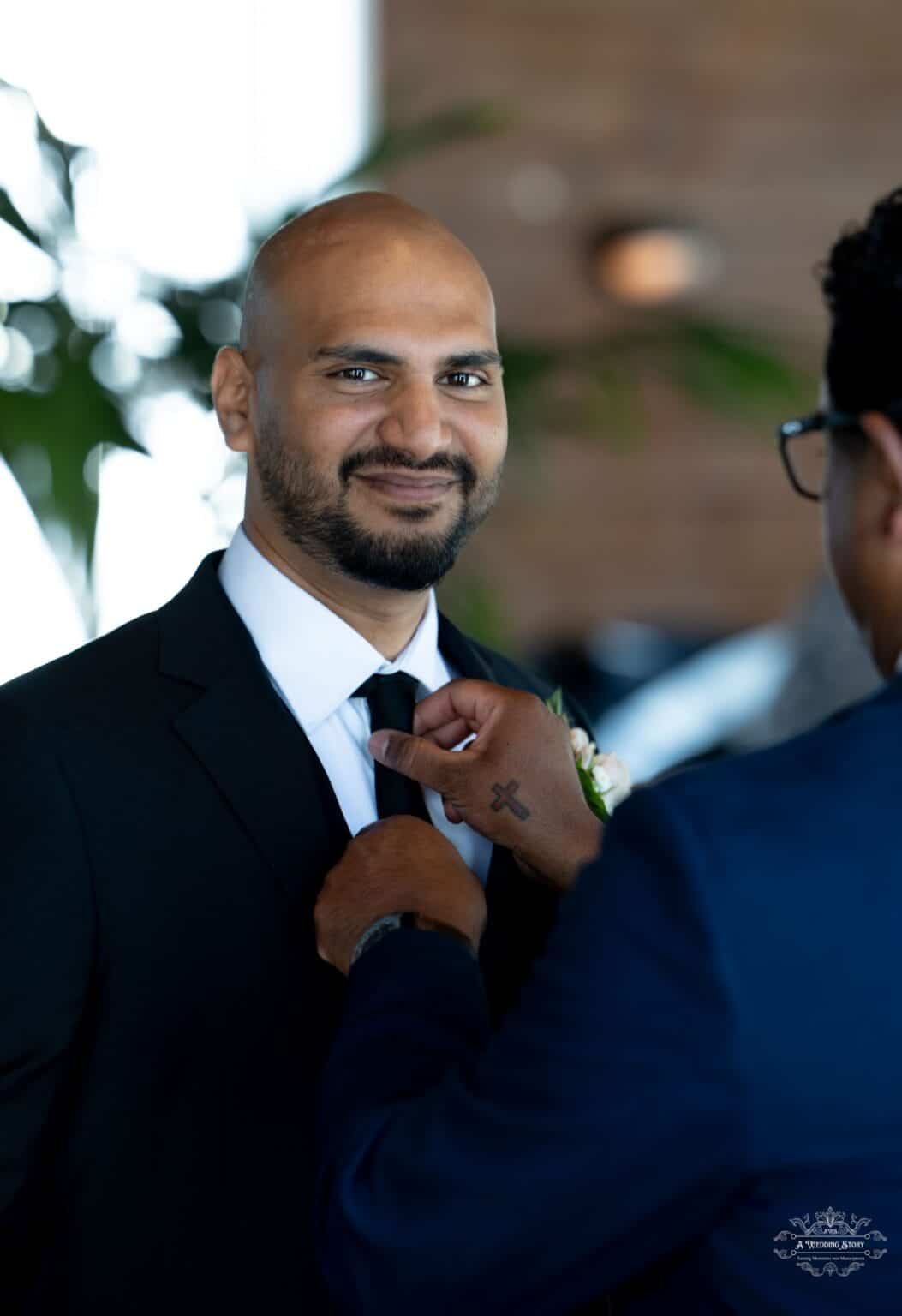 A groom smiling as his best man adjusts his tie before the ceremony, captured in a candid moment by a Wellington wedding photographer