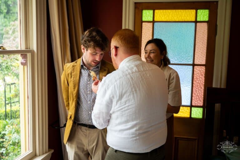 Groom getting his boutonnière pinned before the wedding in Carterton, surrounded by loved ones