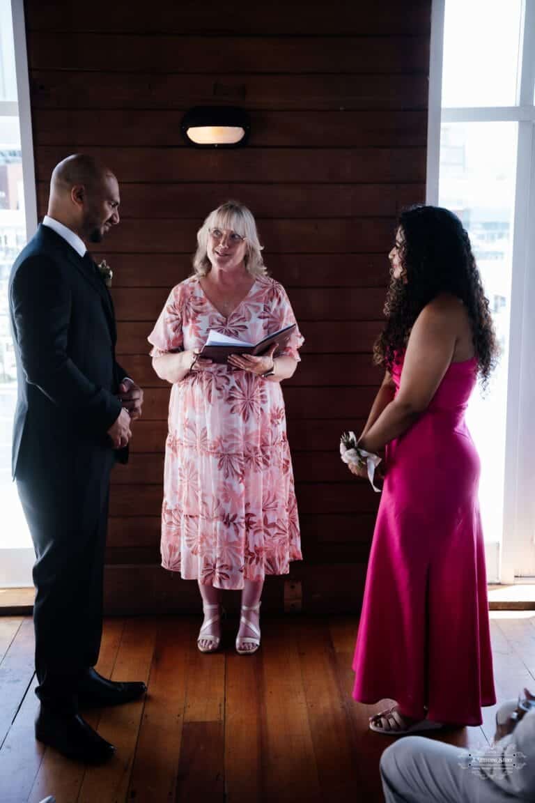 A bride and groom standing before their wedding officiant during an intimate indoor ceremony, exchanging meaningful vows in Wellington