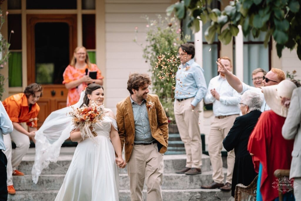 Bride and groom walking hand in hand as guests throw confetti at their Carterton home wedding celebration.