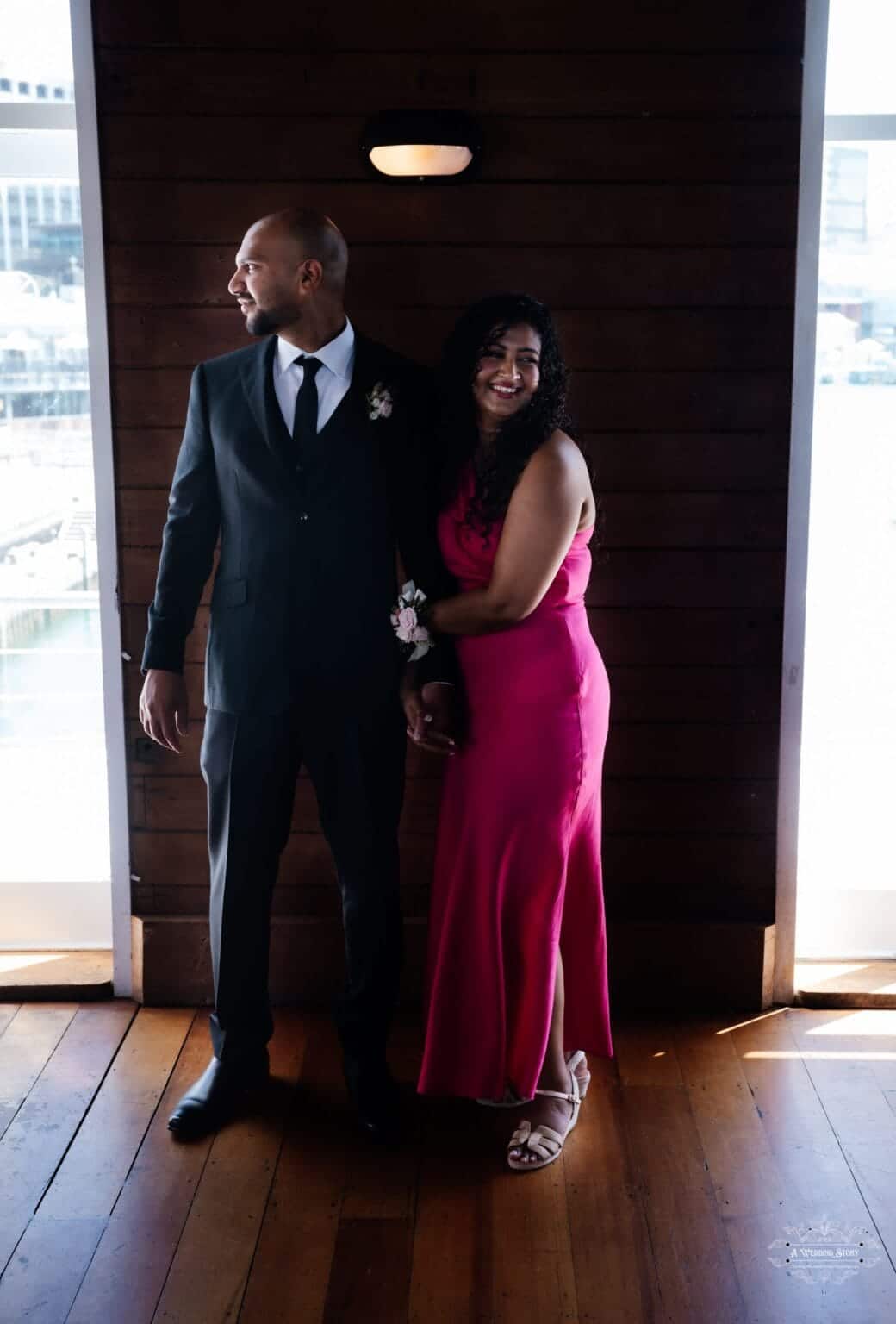 A newlywed couple sharing a candid moment, holding hands and smiling, captured in warm indoor lighting at their Wellington wedding